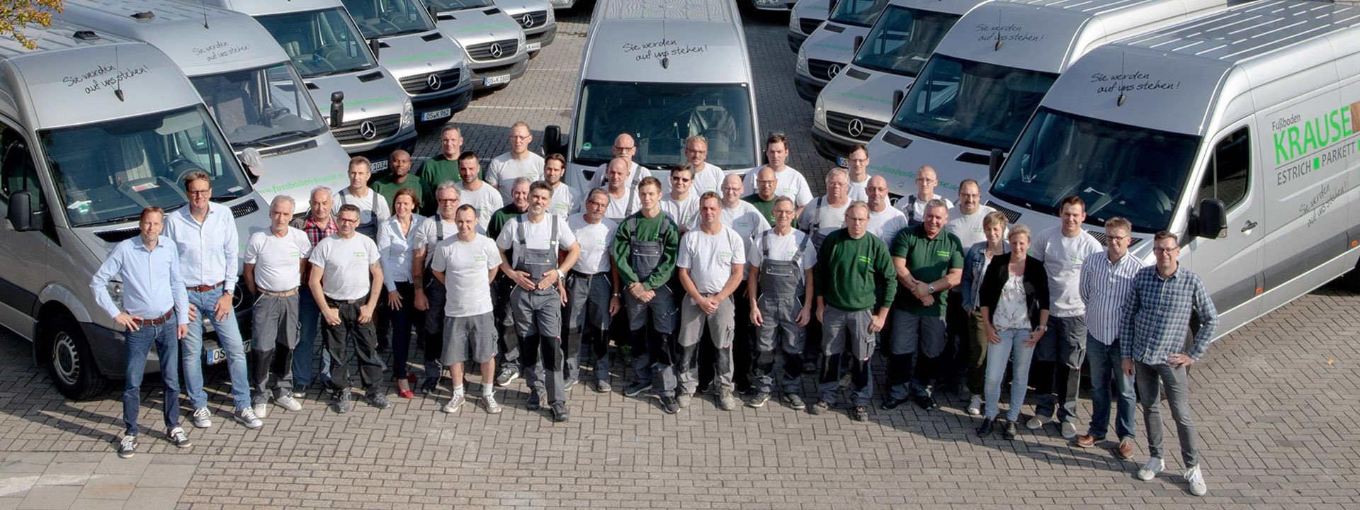 Gruppenfoto der Mitarbeiter von Fu&szlig;boden Krause vor Firmenfahrzeugen auf dem Betriebshof
