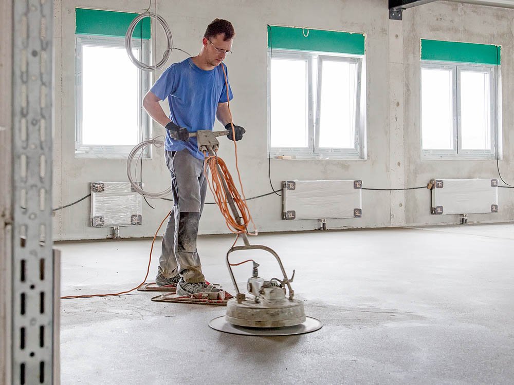 Maschinelle Estrichbearbeitung im Innenbereich Mitarbeiter glättet frisch eingebrachten Estrich mit einer Glättmaschine